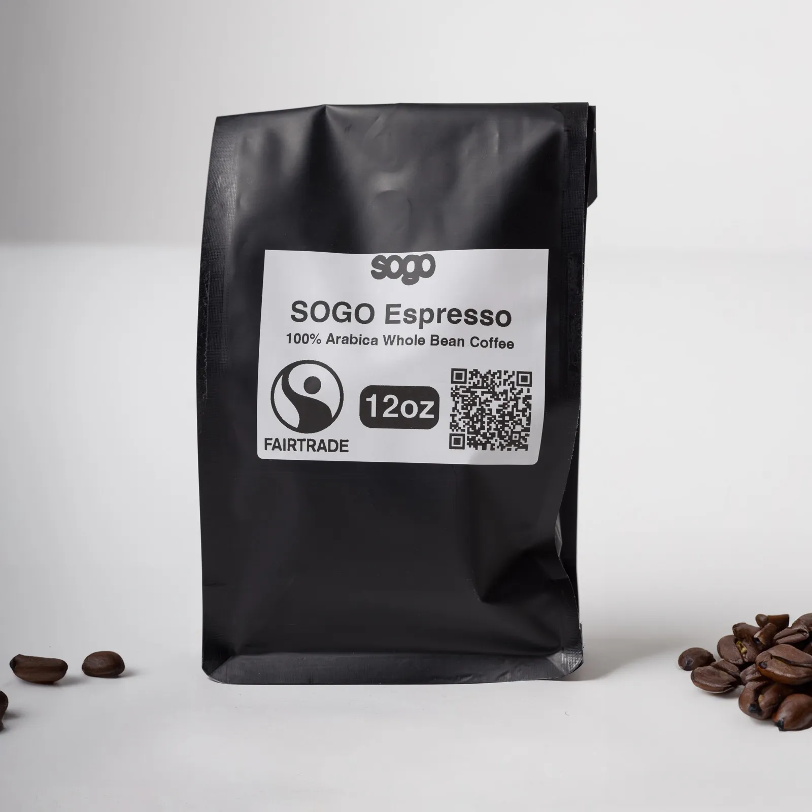 A black 12 oz bag of SOGO Espresso whole bean coffee, beside scattered roasted beans.